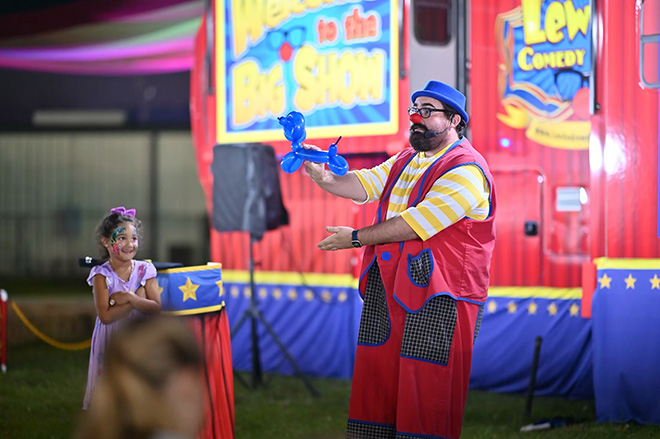 Lew-E the clown creates a balloon animal while a little girl watches