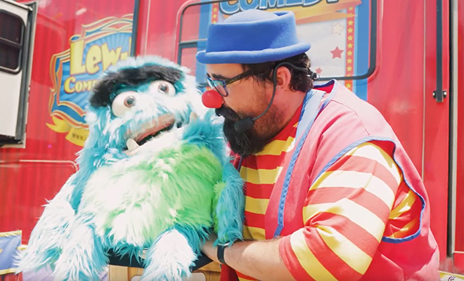 Lew-E the clown talks to his blue and green furry puppet