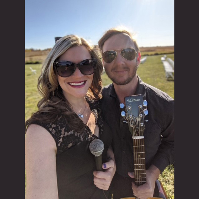 Matt & Sara pose outdoors with a microphone and acoustic guitar