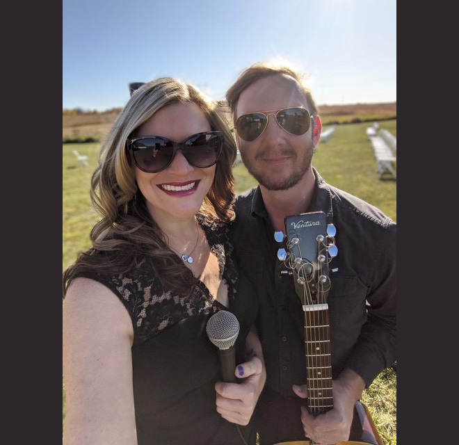 Matt & Sara pose outdoors with a microphone and acoustic guitar