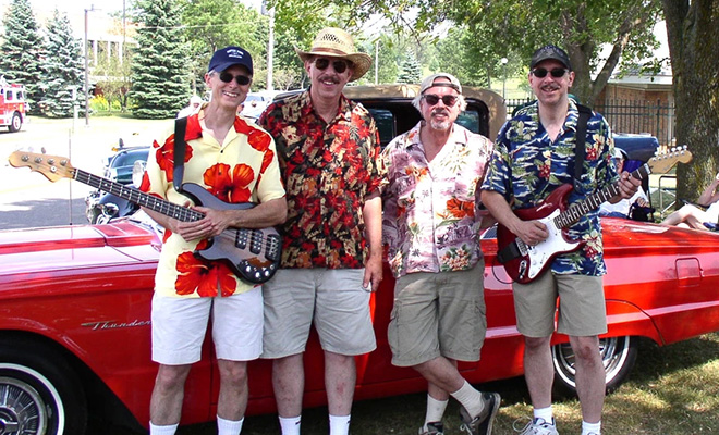 The Castaways band poses with a red vintage car