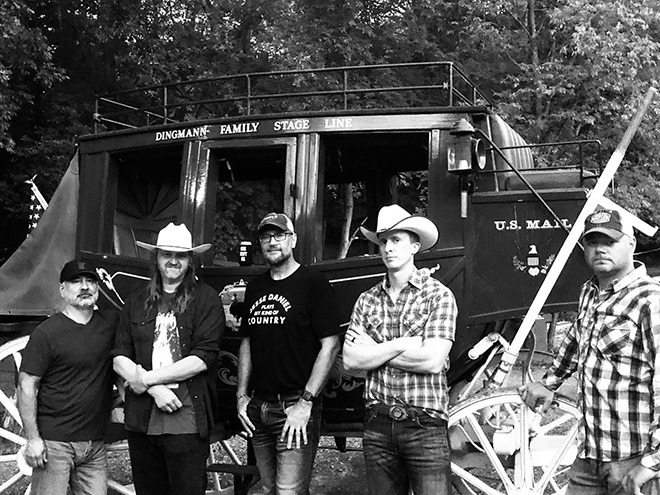 members of the band Gus Sent Me pose with an antique stage coach