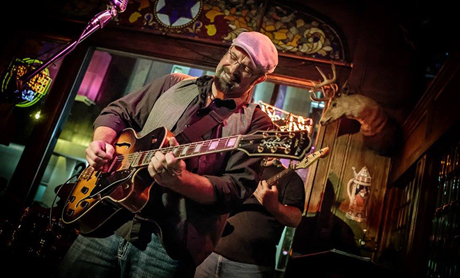 Jason Paulson smiling and playing guitar