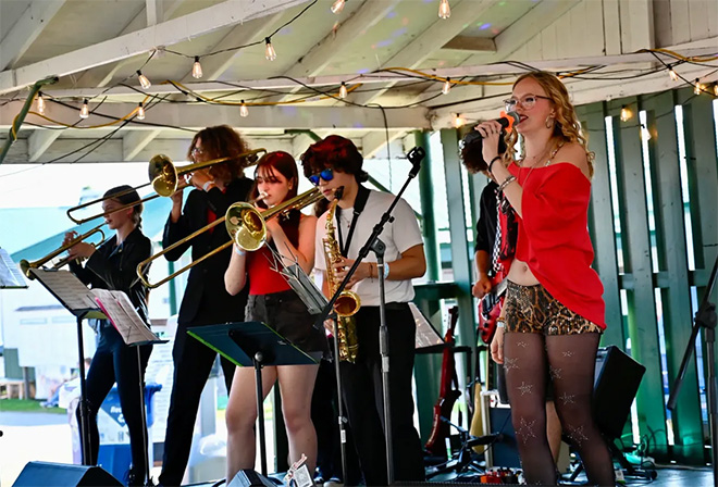 Sparrow Road performs: a singer in a red shirt and four horns play on the Carver County Fair Patio stage